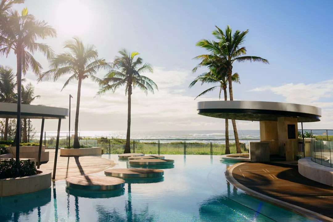 A photo of the pool at the Gold Coast Langham - clear water looking out over the ocean, blue skies and palm trees: a tropical paradise